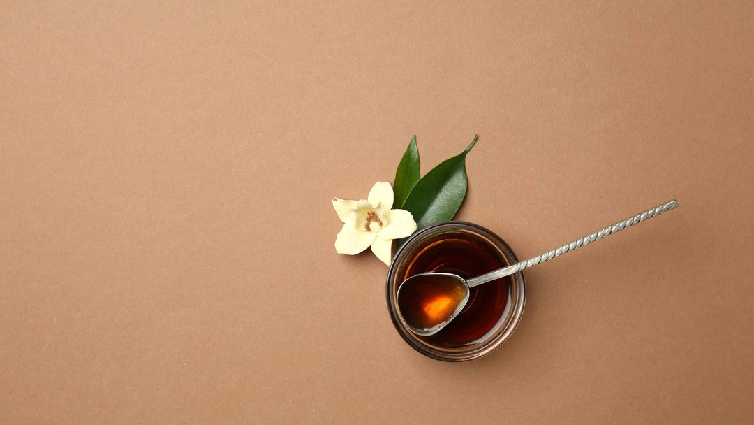 Vanilla extract in a bowl with a vanilla flower on a light brown canvas.