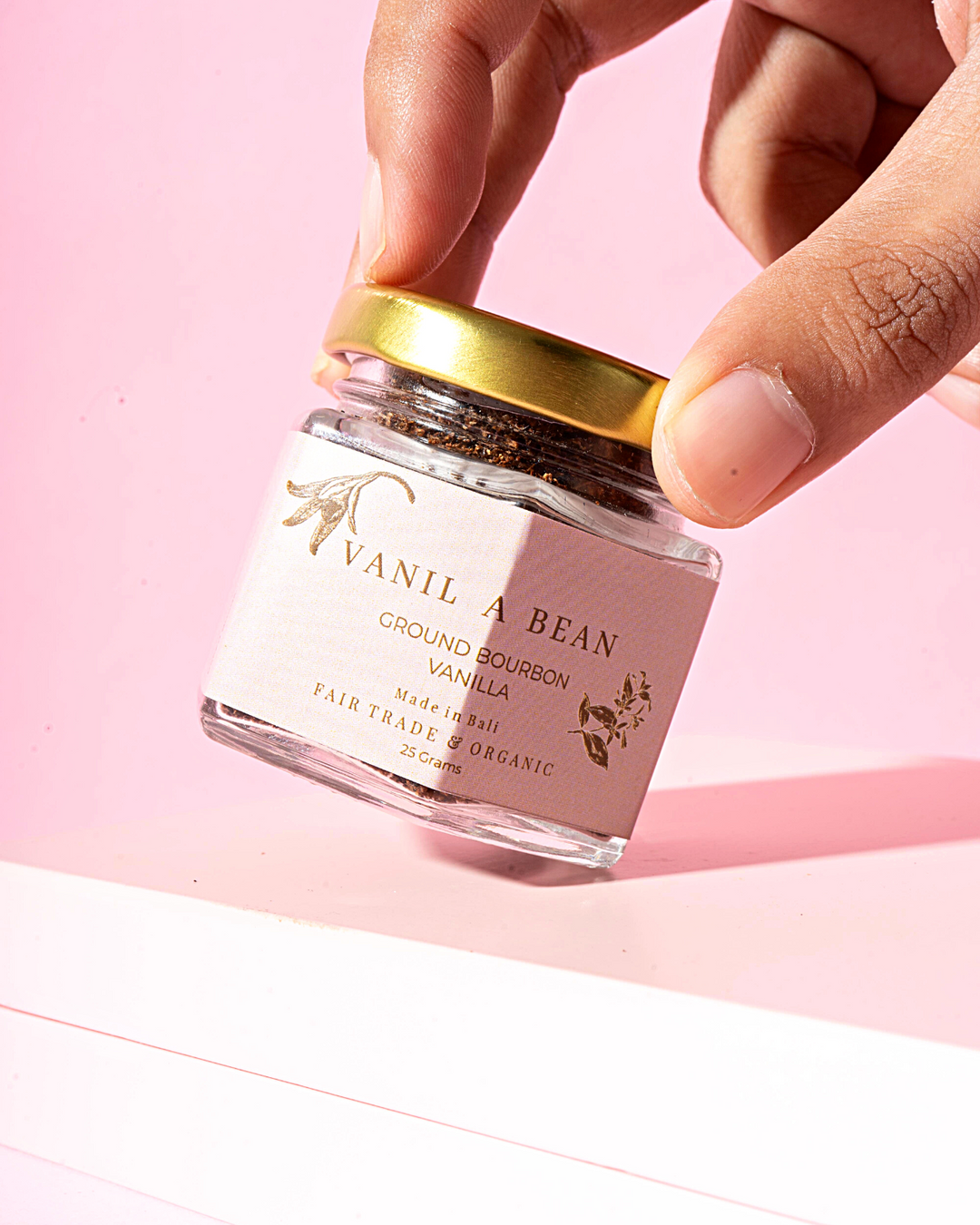 Vanil a bean's ground bourbon powder being held in a hand on a pink background