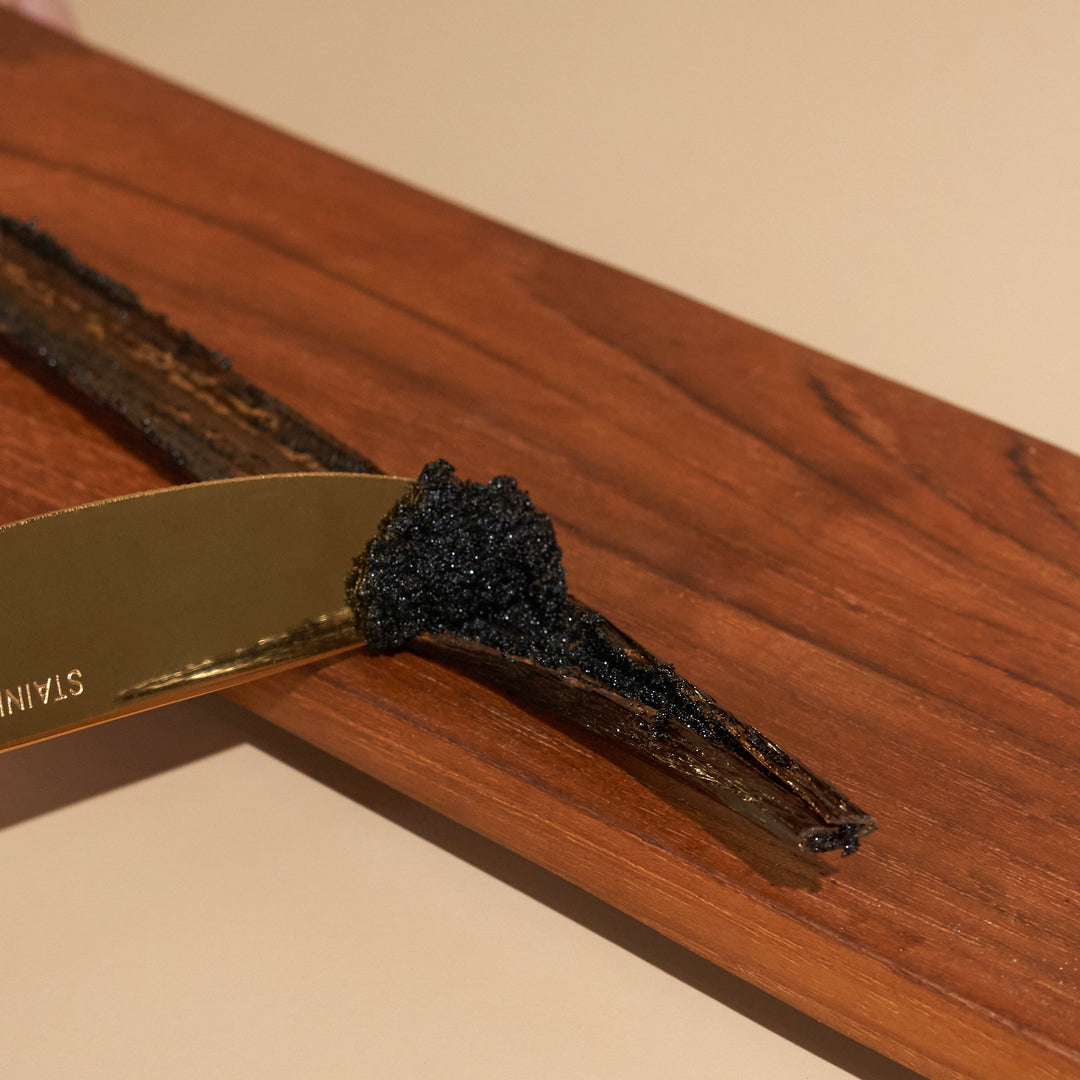 Knife scraping our grade a tahitian vanilla bean split open full of dark vanilla seeds