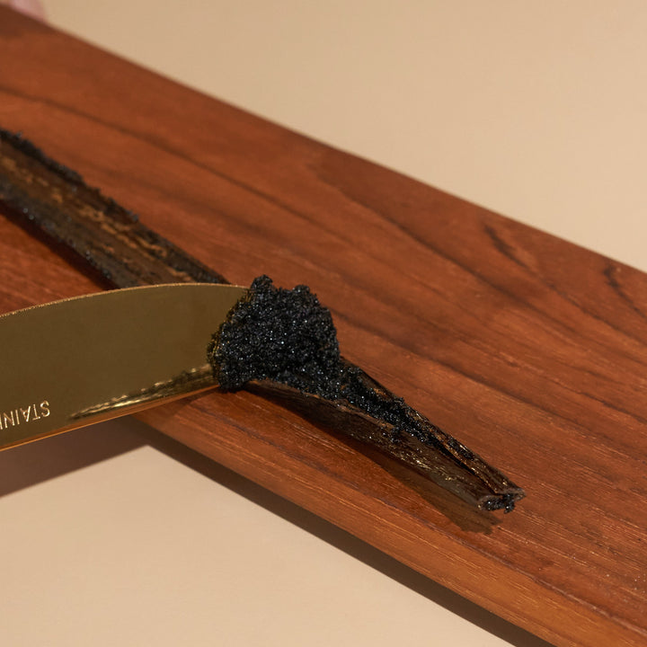 Knife scraping our grade a tahitian vanilla bean split open full of dark vanilla seeds