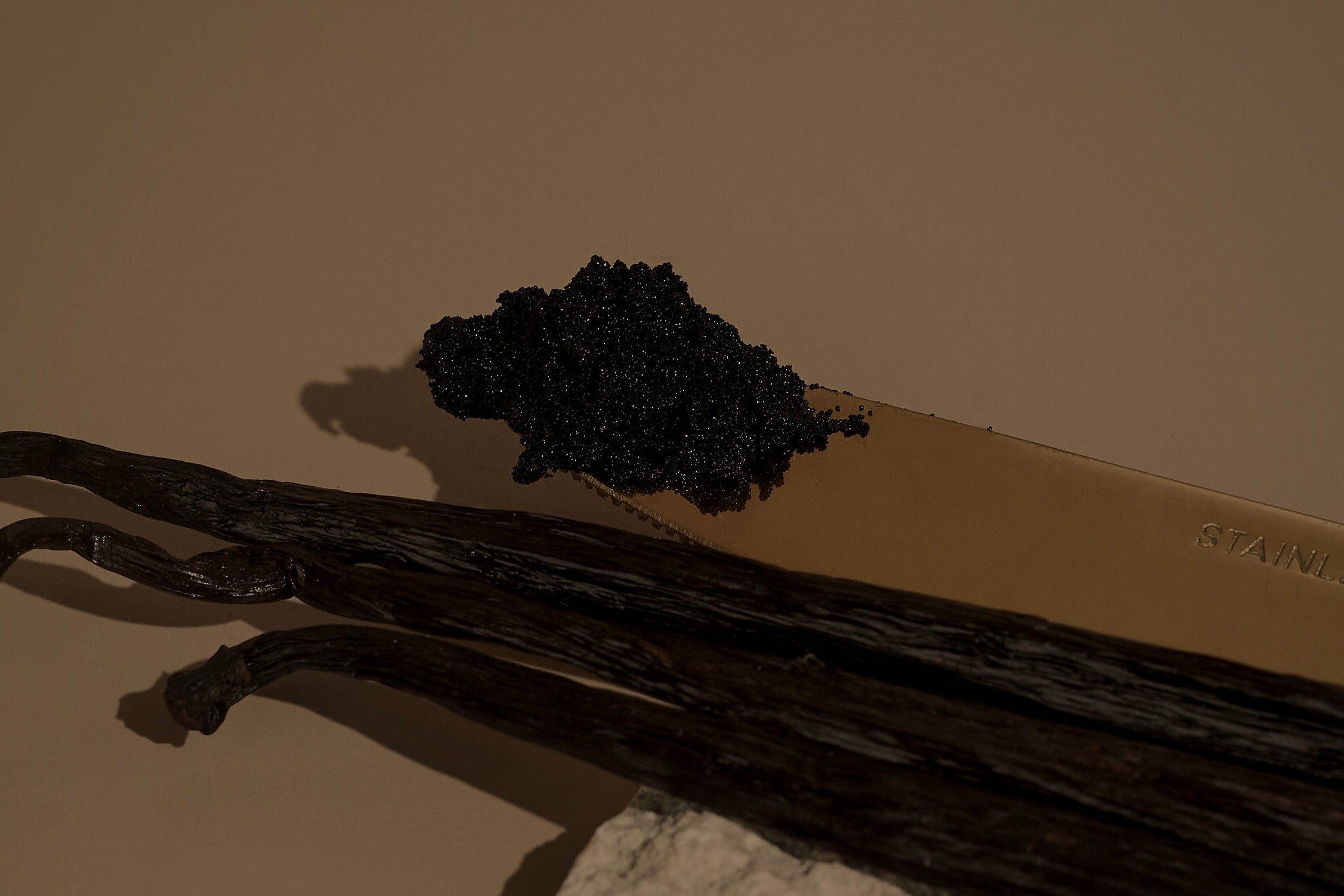 Vanilla caviar on a knife beside whole Bourbon vanilla beans